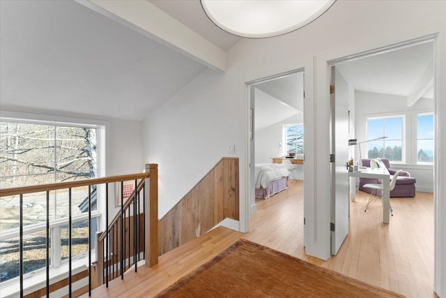 hall featuring lofted ceiling with beams, an upstairs landing, light wood-style flooring, and plenty of natural light