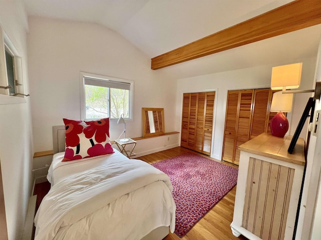 bedroom with multiple closets, wood finished floors, and vaulted ceiling