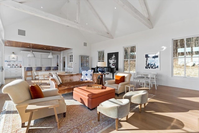 living area featuring a wealth of natural light, visible vents, high vaulted ceiling, wood finished floors, and beamed ceiling