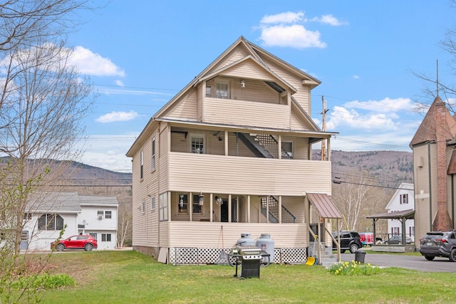 rear view of property with a mountain view, a balcony, and a lawn