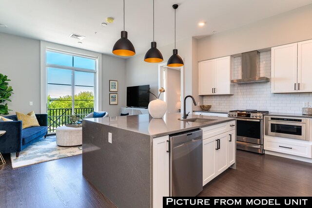 kitchen with appliances with stainless steel finishes, backsplash, wall chimney exhaust hood, and dark wood-type flooring