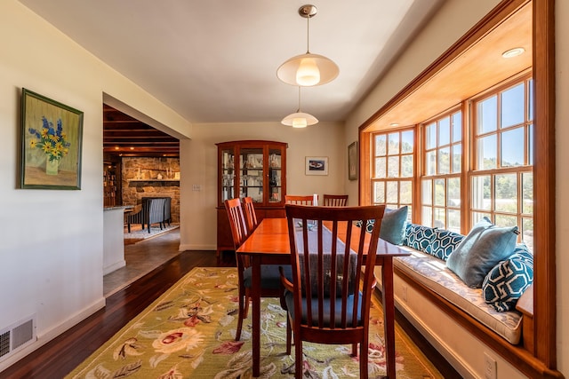 dining room with a stone fireplace and dark wood-type flooring