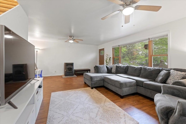 living room featuring light hardwood / wood-style flooring, ceiling fan, and a wood stove