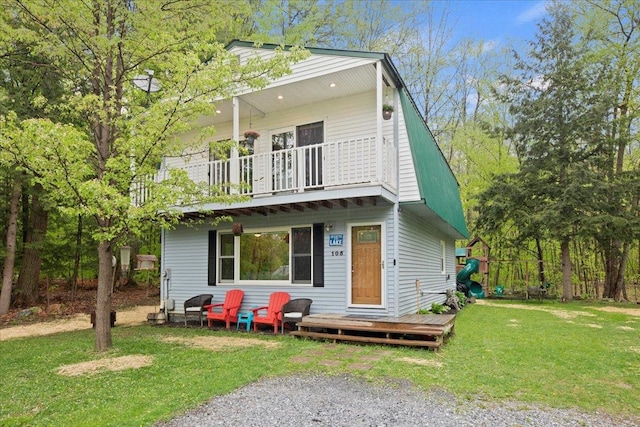 back of house with a balcony, a playground, and a lawn