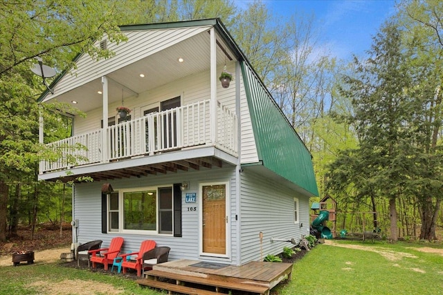 back of property with a yard, a balcony, and a playground