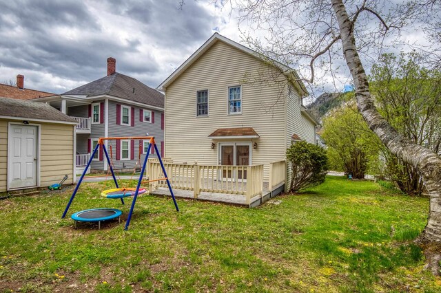 back of property featuring a playground, a deck, and a lawn