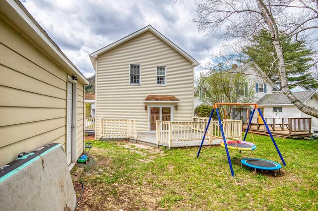 back of property featuring a playground, a deck, and a lawn