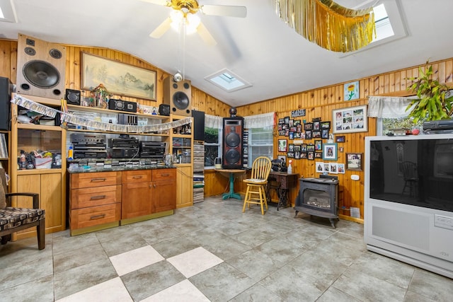 interior space featuring ceiling fan, lofted ceiling with skylight, light tile floors, a wood stove, and wood walls