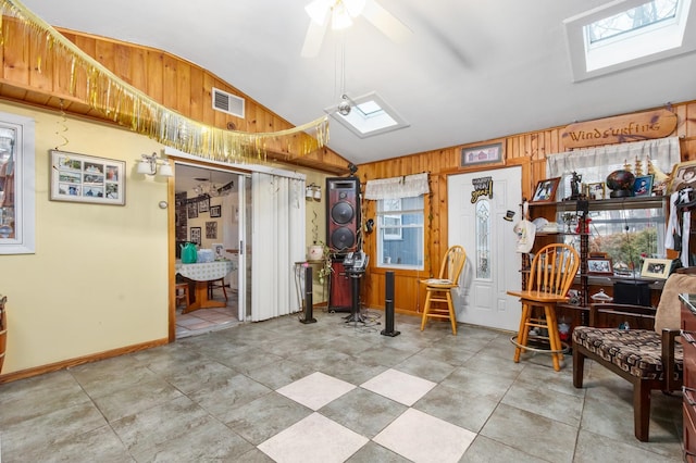 miscellaneous room featuring ceiling fan, tile flooring, wood walls, and vaulted ceiling with skylight