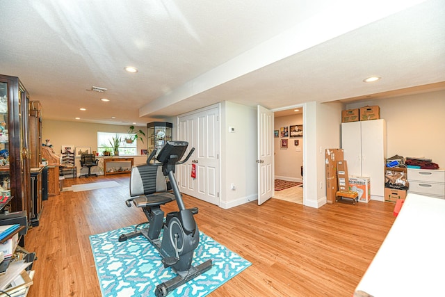 exercise area with light wood-type flooring and a textured ceiling