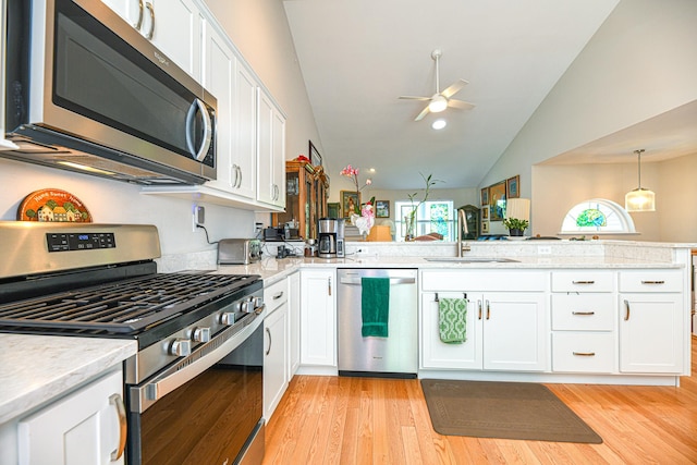 kitchen featuring appliances with stainless steel finishes, light wood-type flooring, vaulted ceiling, sink, and white cabinetry