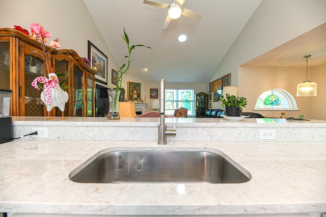 kitchen featuring ceiling fan, sink, light stone counters, pendant lighting, and vaulted ceiling