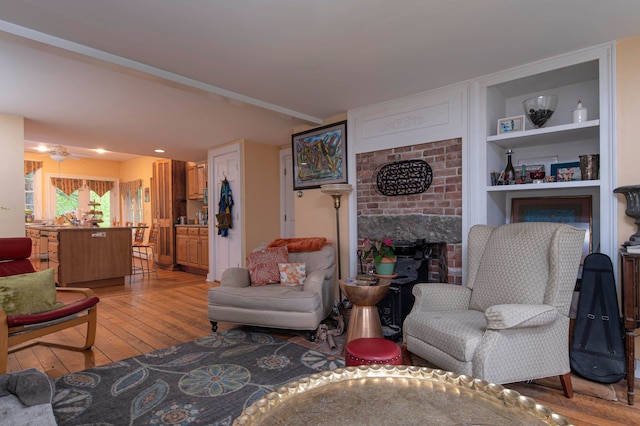 living room with ceiling fan, built in shelves, and light hardwood / wood-style flooring