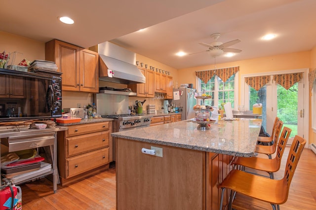 kitchen with a kitchen bar, light hardwood / wood-style flooring, wall chimney exhaust hood, and stainless steel appliances