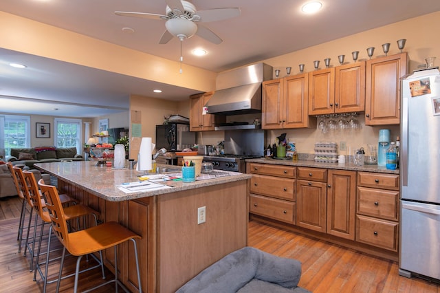 kitchen featuring stainless steel appliances, light hardwood / wood-style flooring, a center island with sink, and wall chimney range hood