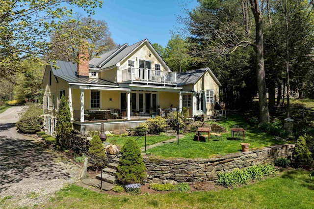 rear view of house featuring a porch, a balcony, and a lawn