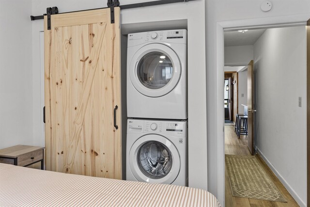 laundry area featuring a barn door, hardwood / wood-style floors, and stacked washer and clothes dryer