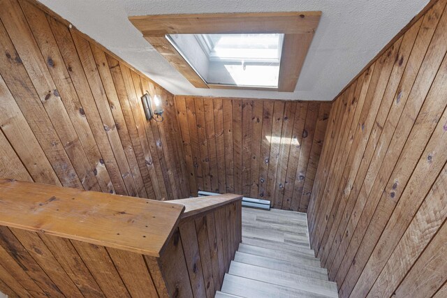 stairs with wood walls, light wood-type flooring, and a skylight