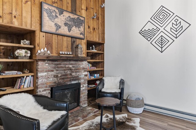 living area featuring baseboard heating, wooden walls, a brick fireplace, and dark wood-type flooring