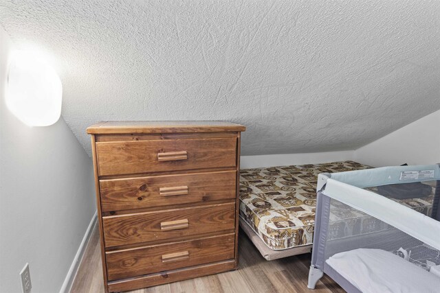 bedroom with vaulted ceiling, a textured ceiling, and hardwood / wood-style flooring