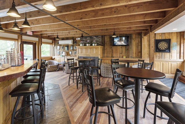 dining space featuring beamed ceiling, hardwood / wood-style flooring, wood walls, and a wall mounted air conditioner