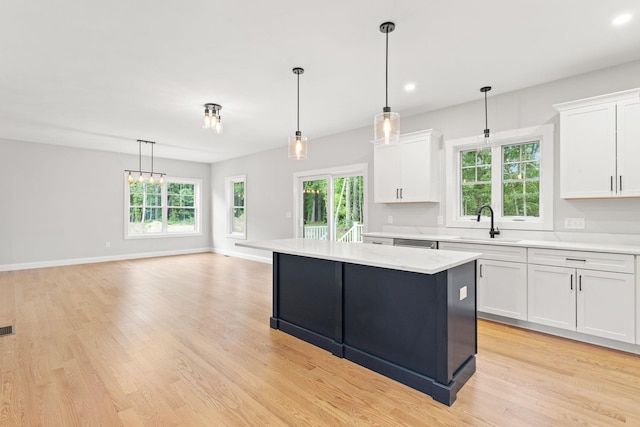 kitchen with a sink, a kitchen island, white cabinets, and light countertops