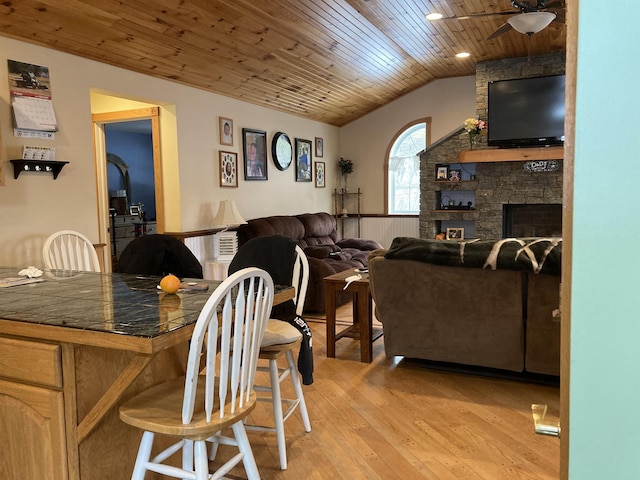 dining space featuring ceiling fan, vaulted ceiling, light wood-style flooring, wooden ceiling, and a fireplace