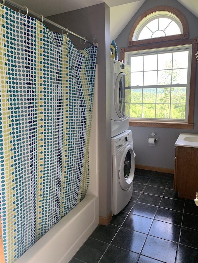 washroom with stacked washer and clothes dryer, baseboards, and dark tile patterned flooring