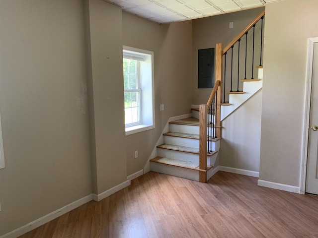 staircase featuring electric panel, wood finished floors, and baseboards