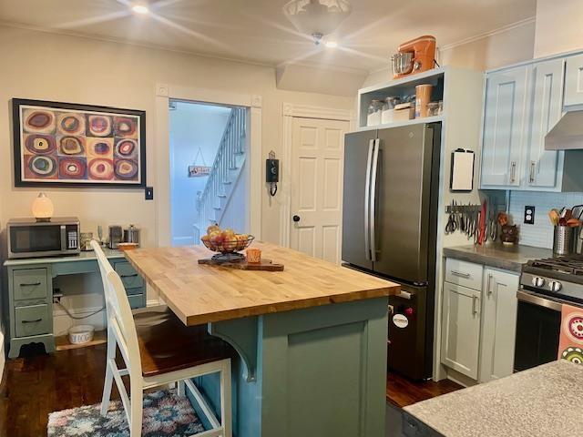 kitchen featuring a breakfast bar area, appliances with stainless steel finishes, wood counters, dark hardwood / wood-style flooring, and a kitchen island