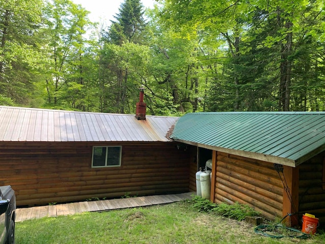 view of property exterior featuring a chimney, log veneer siding, and metal roof