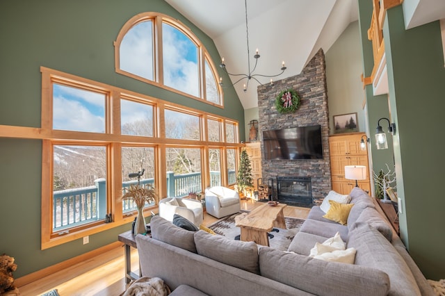 living room featuring a stone fireplace, high vaulted ceiling, light hardwood / wood-style floors, and an inviting chandelier