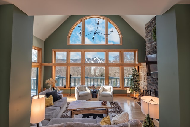 living room featuring a stone fireplace, high vaulted ceiling, light hardwood / wood-style floors, and a notable chandelier