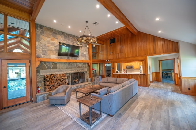 living room with beam ceiling, a stone fireplace, high vaulted ceiling, a chandelier, and light wood-type flooring