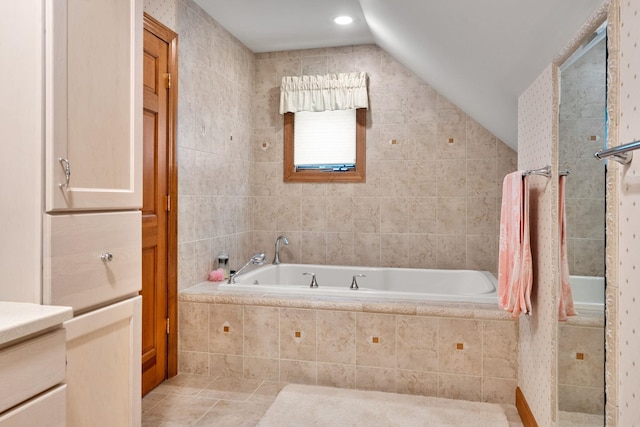 full bathroom with lofted ceiling, tile patterned floors, tile walls, and tiled bath