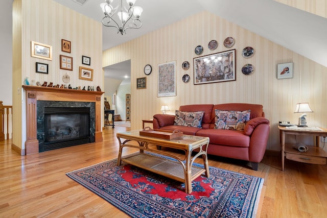 living room featuring wood finished floors, wallpapered walls, a premium fireplace, a chandelier, and vaulted ceiling