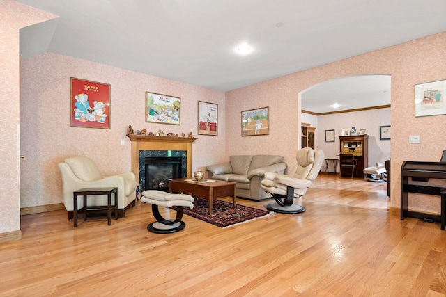 living area with baseboards, light wood finished floors, wallpapered walls, arched walkways, and a high end fireplace