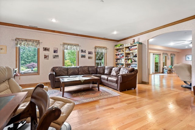 living room featuring ceiling fan, arched walkways, light wood-type flooring, and ornamental molding