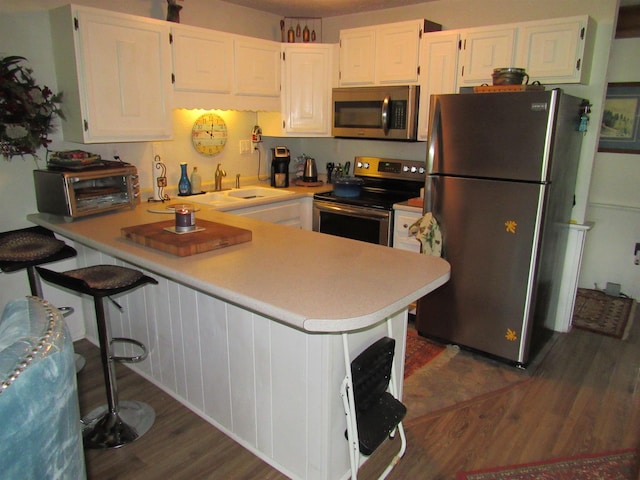 kitchen with kitchen peninsula, a kitchen bar, stainless steel appliances, sink, and white cabinets