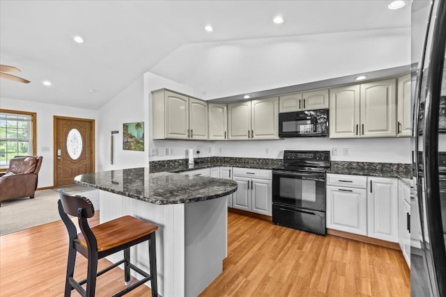 kitchen featuring a kitchen breakfast bar, gray cabinetry, black appliances, light hardwood / wood-style flooring, and dark stone countertops