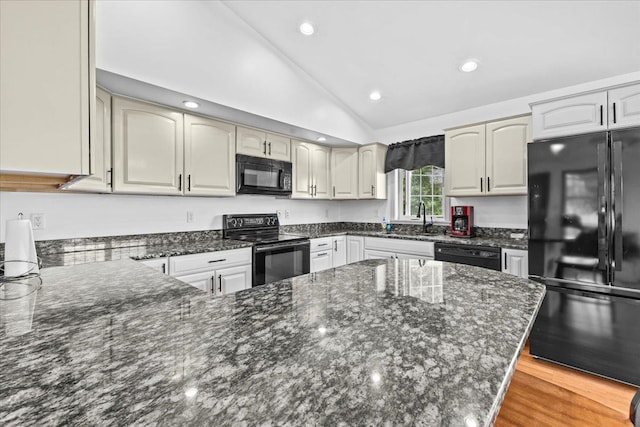 kitchen featuring sink, dark stone counters, lofted ceiling, and black appliances