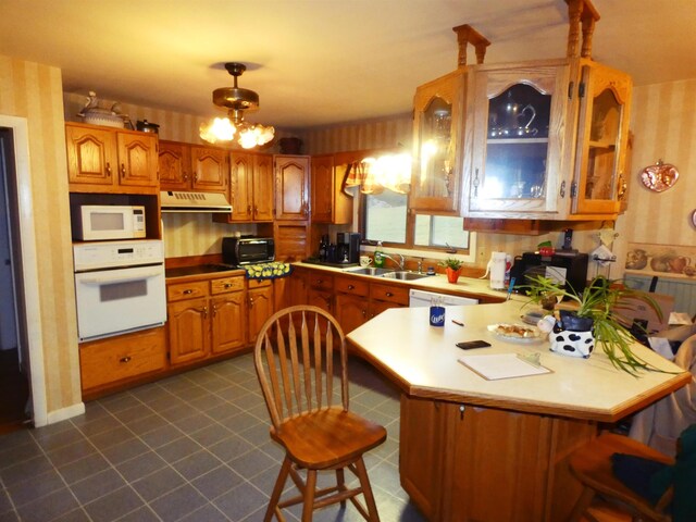 kitchen featuring kitchen peninsula, a kitchen breakfast bar, white appliances, sink, and a chandelier