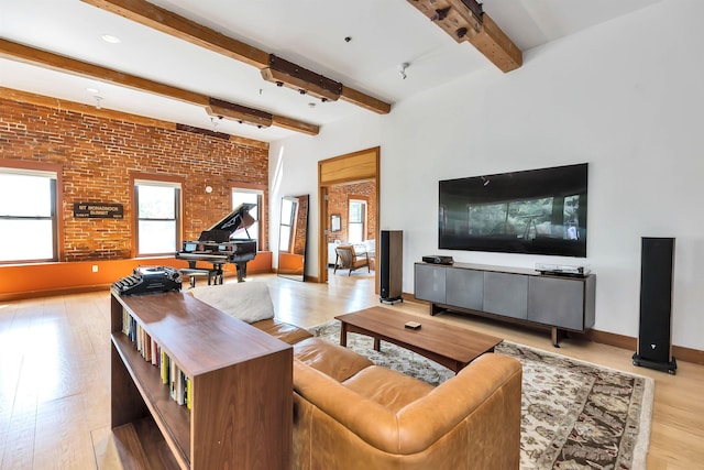 living room featuring a wealth of natural light, beamed ceiling, brick wall, and light hardwood / wood-style floors