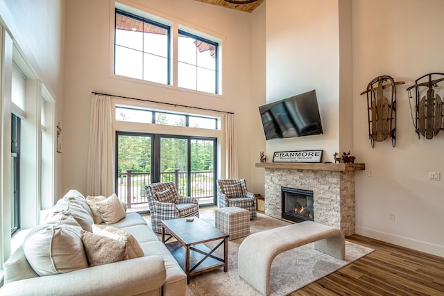 living area featuring a stone fireplace, a high ceiling, baseboards, and wood finished floors