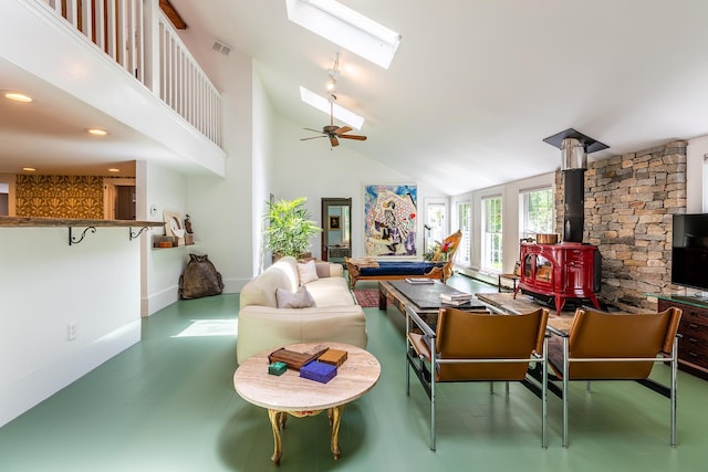 living room with visible vents, ceiling fan, a skylight, a wood stove, and high vaulted ceiling