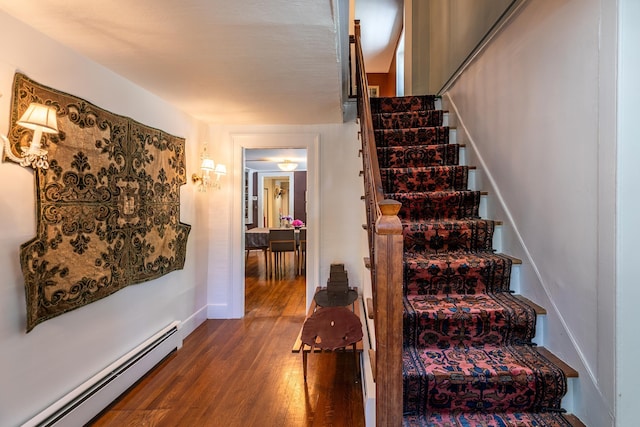 stairs featuring baseboard heating, baseboards, and wood finished floors