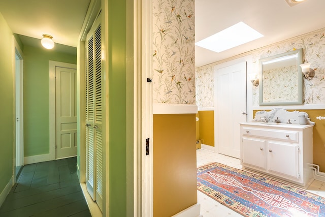 bathroom with a skylight, a wainscoted wall, wallpapered walls, and vanity