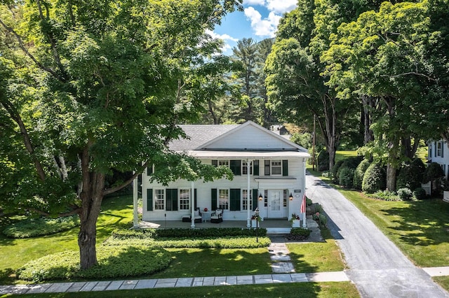 greek revival inspired property featuring covered porch, driveway, and a front lawn
