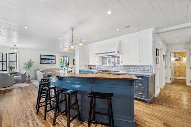 kitchen with custom exhaust hood, wood counters, white cabinets, blue cabinetry, and decorative light fixtures