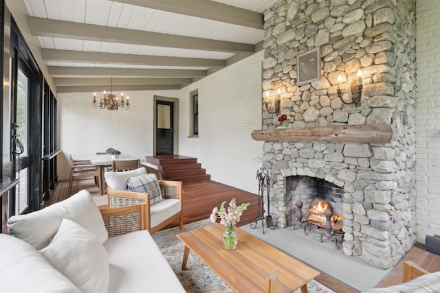 living room featuring hardwood / wood-style flooring, a fireplace, a notable chandelier, beam ceiling, and brick wall